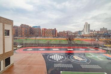 A view of a sports court with various games, city buildings, and an overcast sky.
