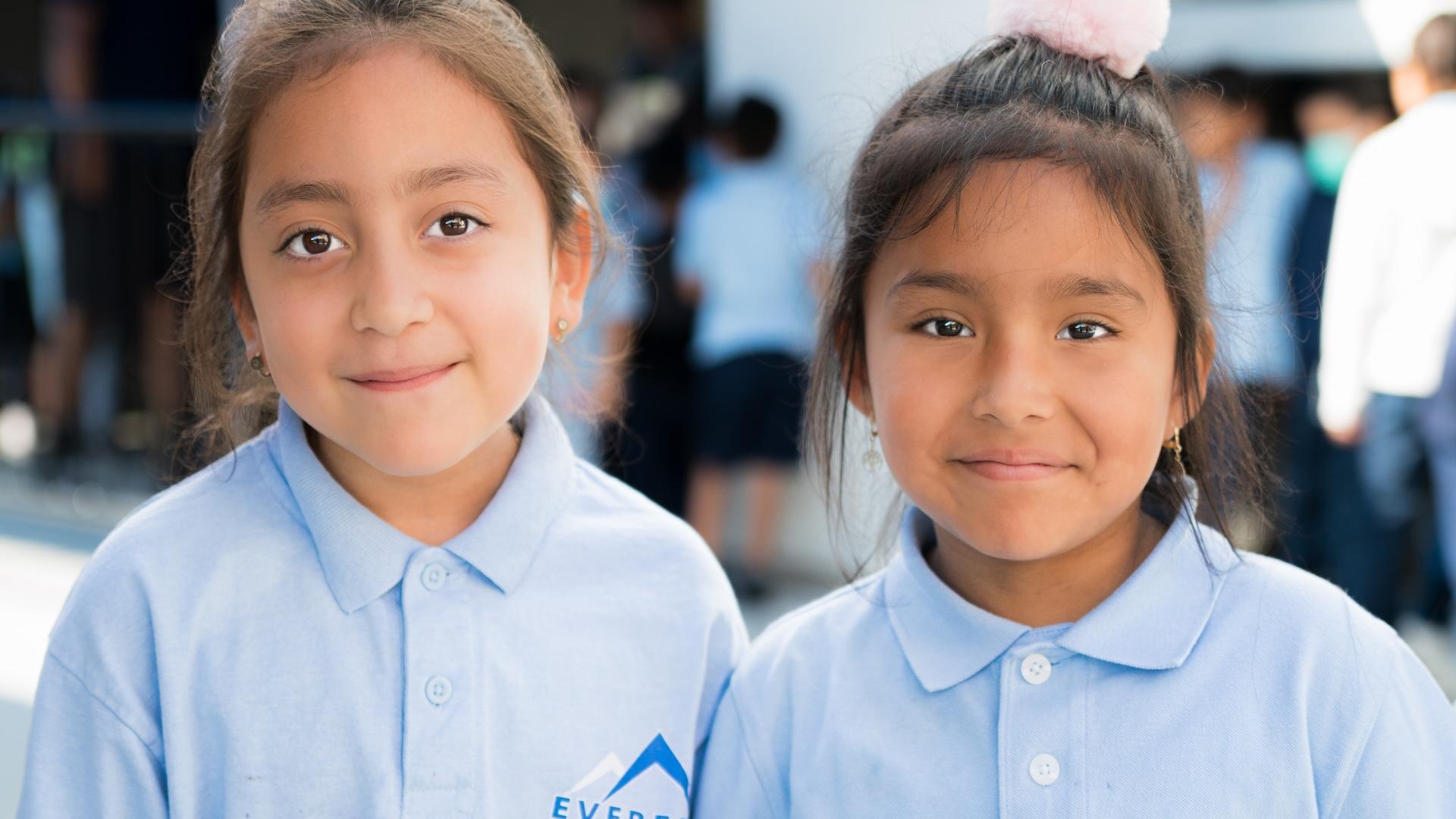 Two girls in matching light blue shirts smile at the camera.