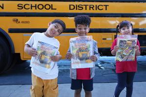 three students with bus safety booklets standing in front of a bus