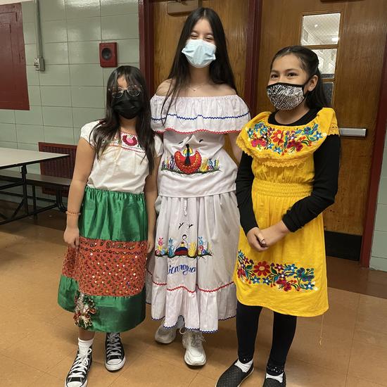 three students standing together wearing brightly colored dresses