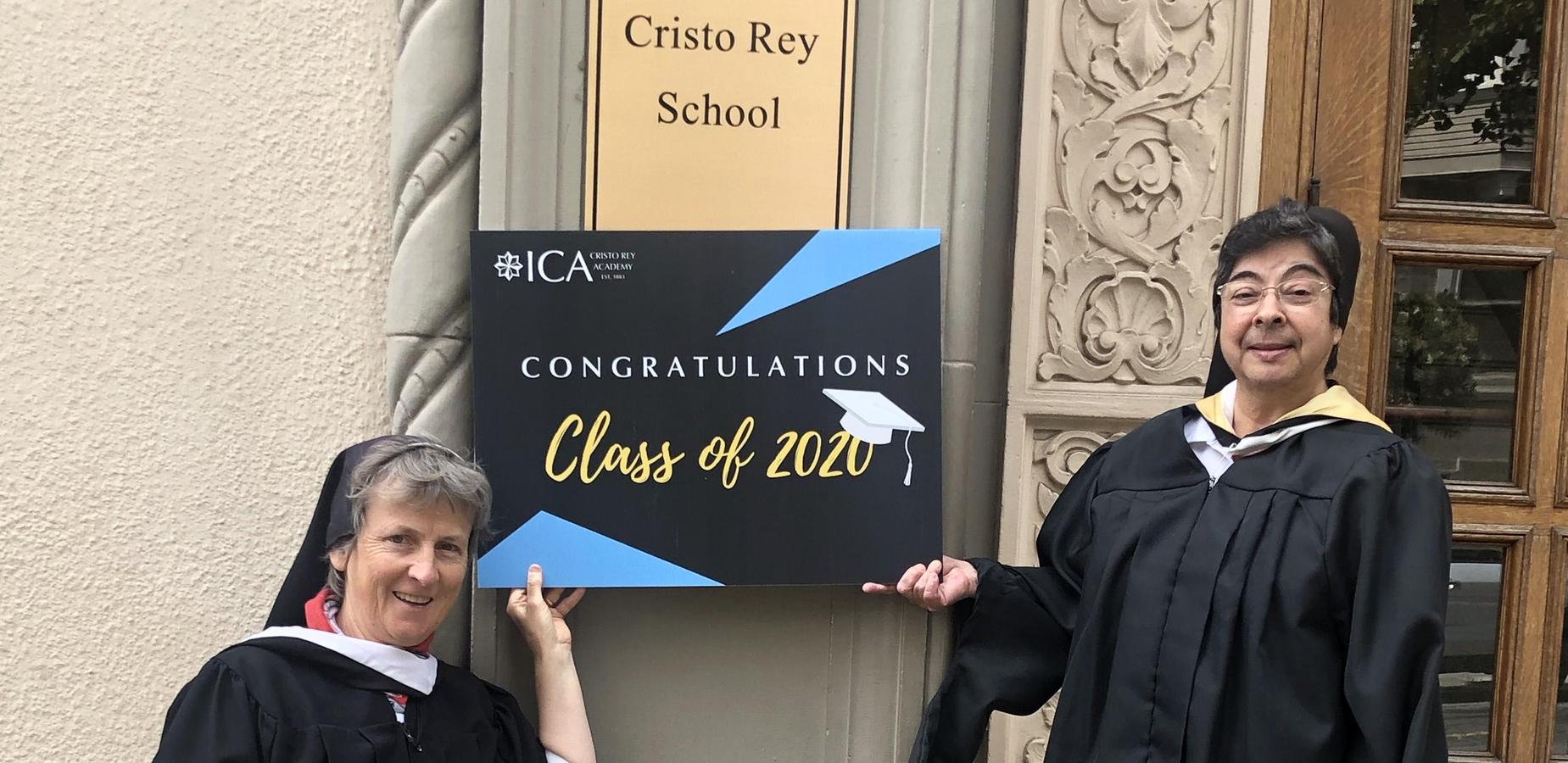Sisters Lilly and Lisa Ann in from of ht eschool building holding a congratulatory sign for the class of 2020
