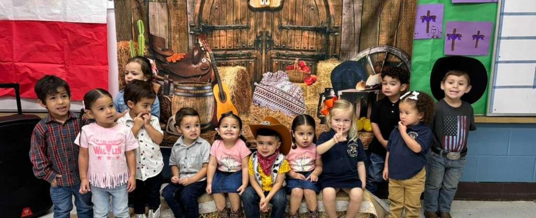 Children posing together in front of a rustic, western-themed backdrop.