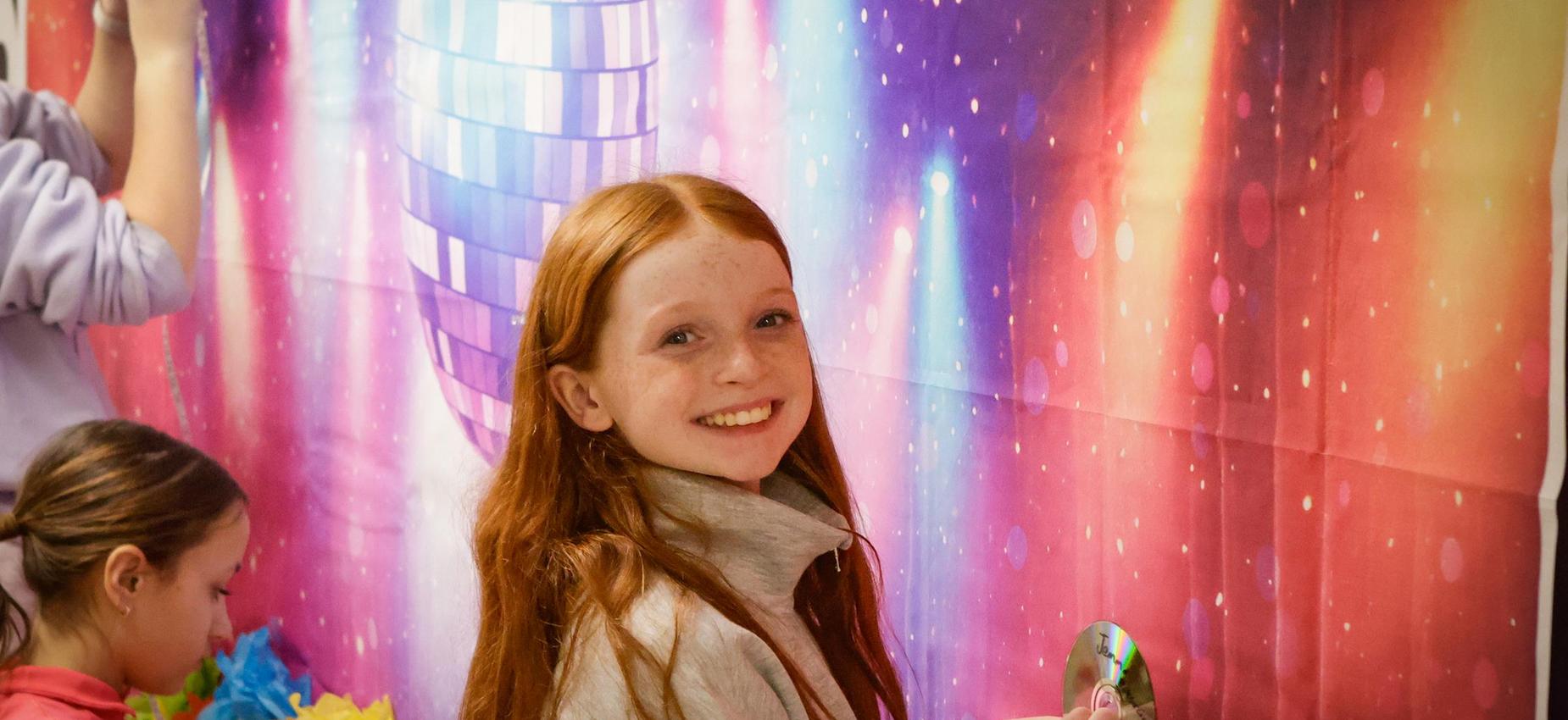 Girl with red hair smiling in front of a colorful backdrop.