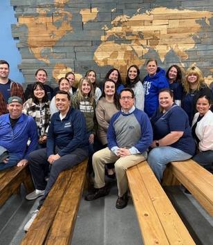 Group of people seated on benches with a world map background.