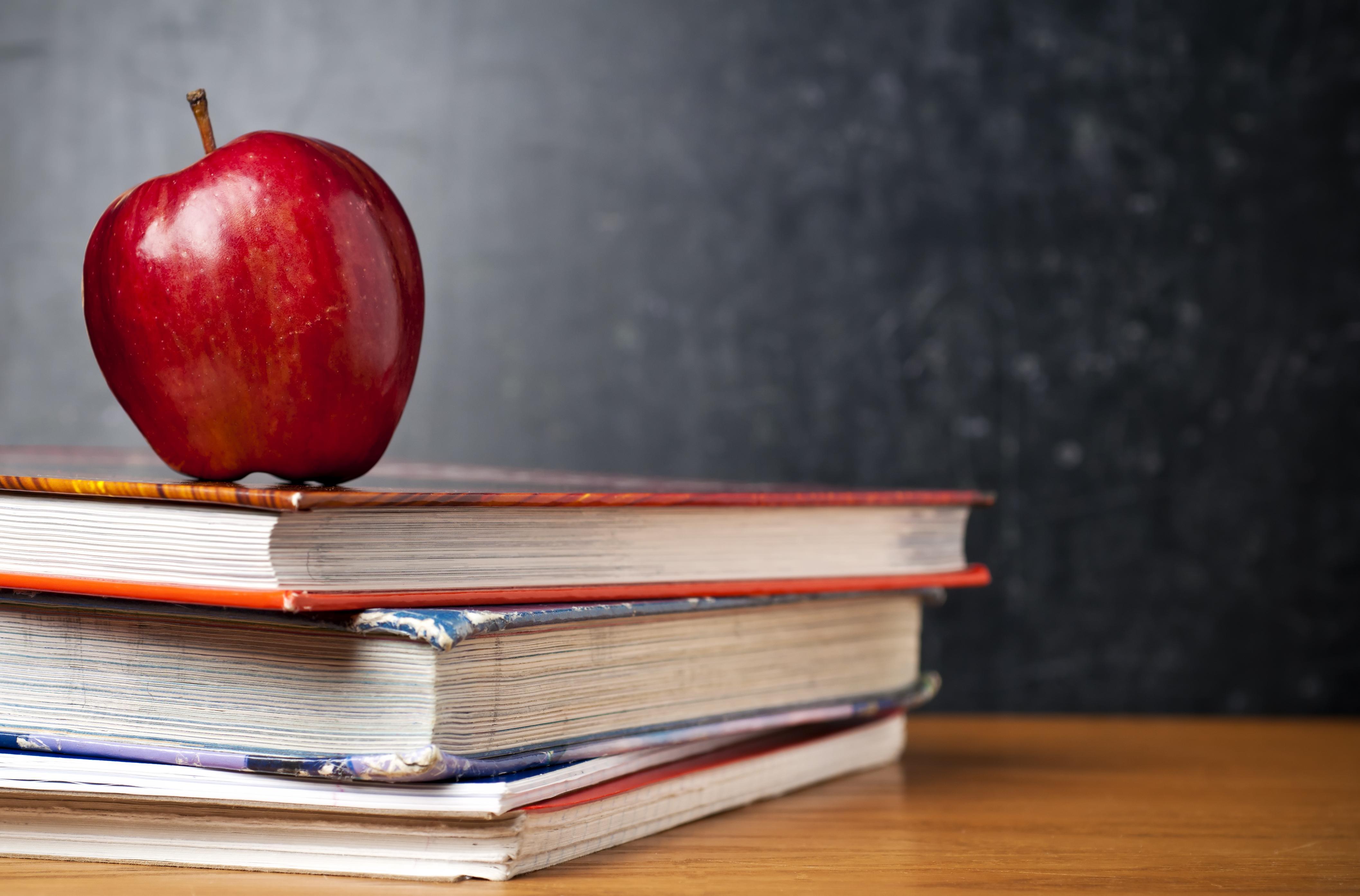 School books on a desk with a red apple.