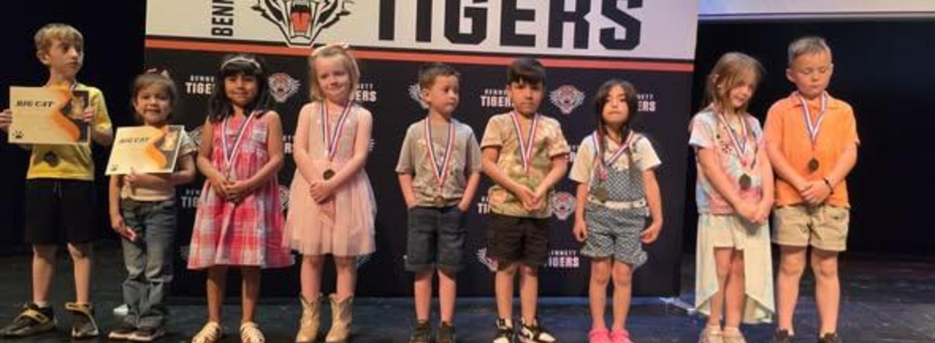 A group of children with medals stand in line at an awards ceremony.