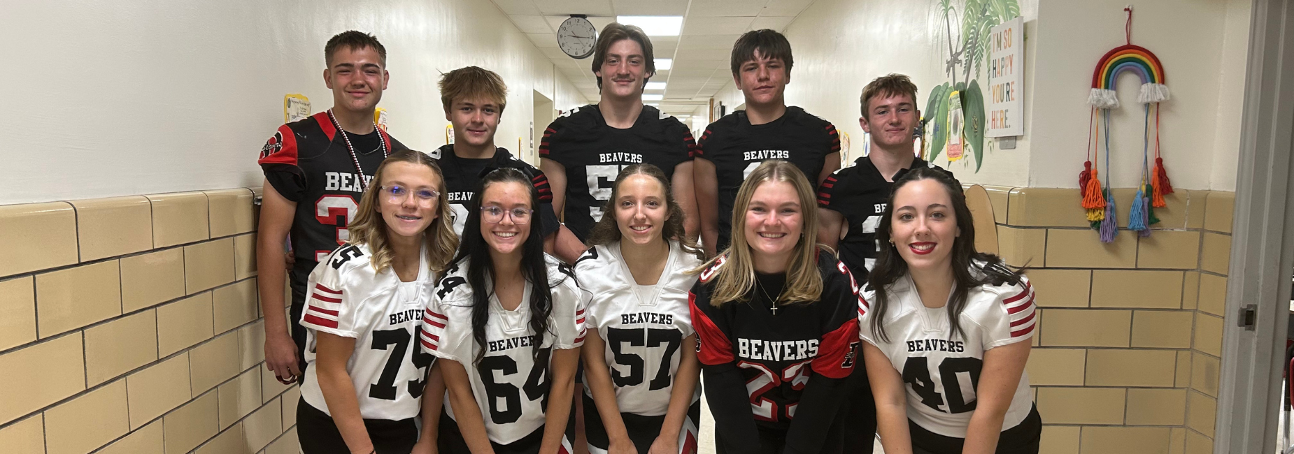 Group of students in Beavers football jerseys smiling in a school hallway.