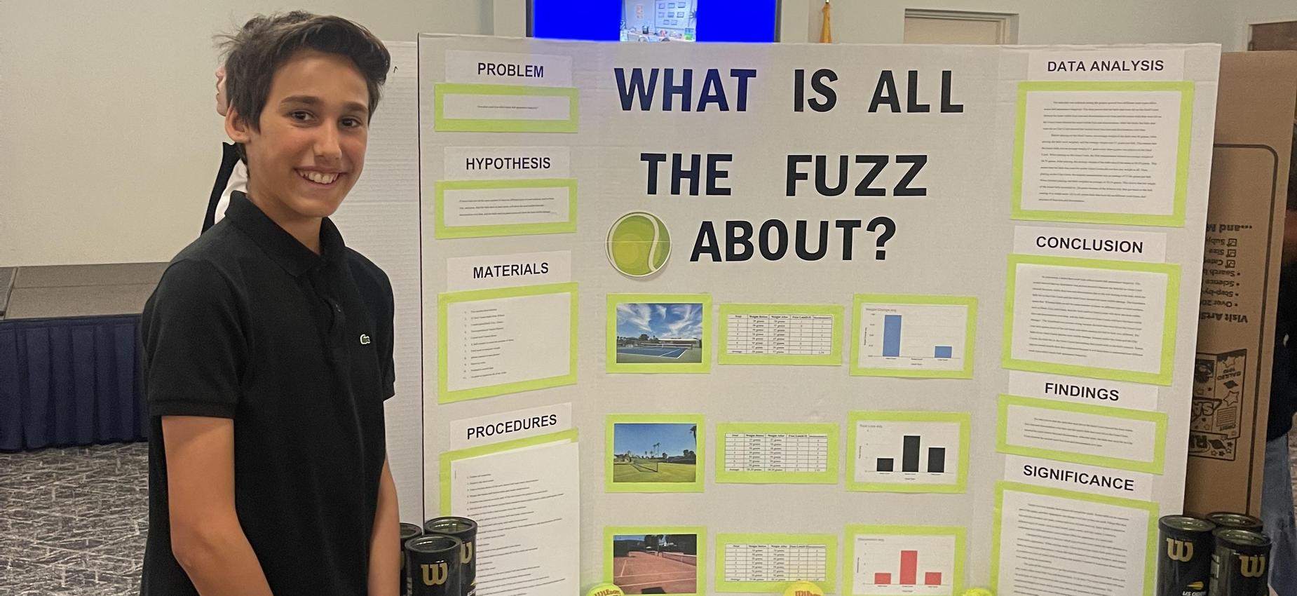 student standing beside science fair board about tennis balls