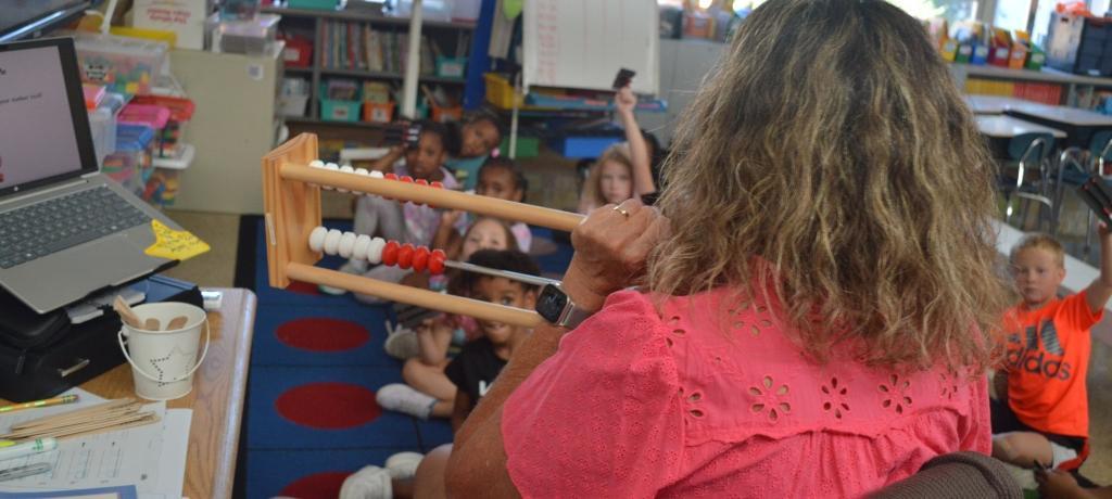 teacher uses abacus to demonstrate math concept as students listen