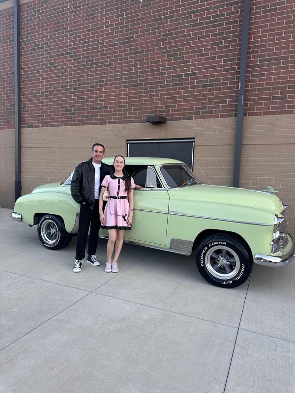 Dad and daughter standing in front of a vintage car.