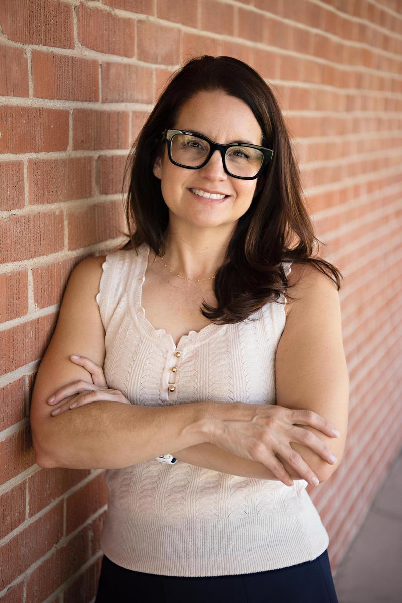 Lupe Lewis in a white shirt and blue skirt with arms crossed against a brick wall