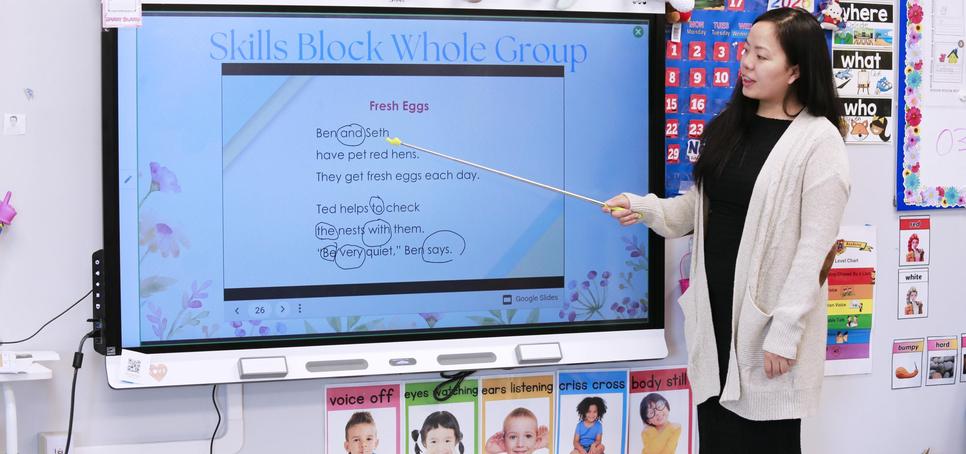 A teacher pointing to a digital board displaying a lesson about fresh eggs.