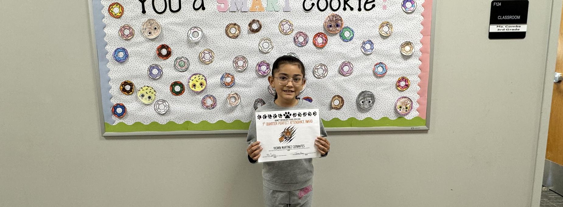 Girl holding an award in front of a cookie-themed bulletin board.