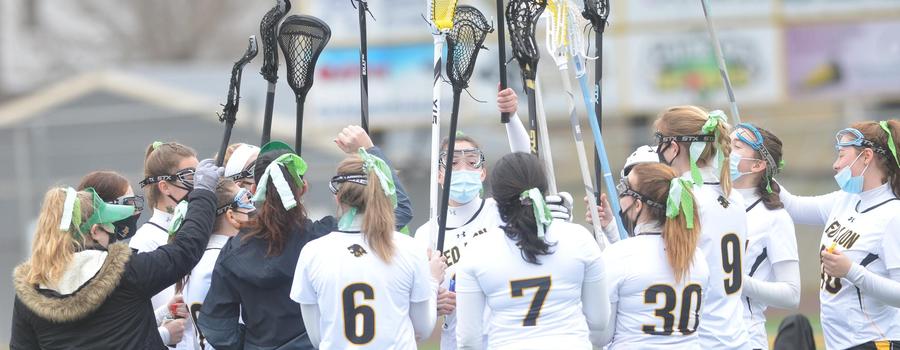 Girls Lacrosse team in a huddle with their sticks in the air.