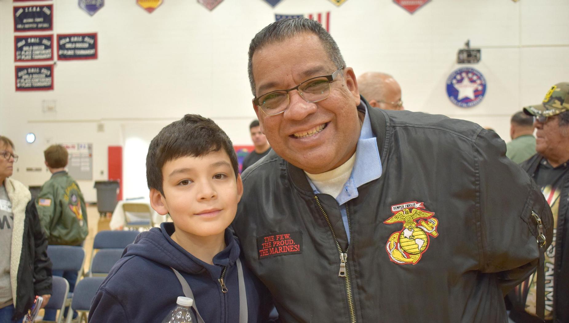 Smiling boy with a bottle of water beside a man in a Marine Corps jacket.