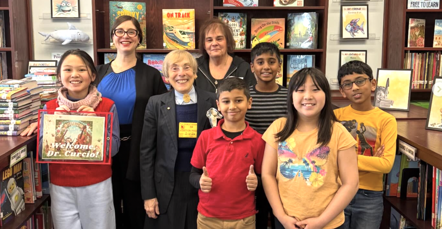 A group of adults and children smiling in a library full of books.