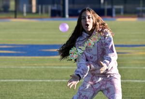 A girl in a lei reaches to catch a pink ball while on the field.