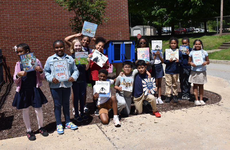 students holding books outside in front of little library