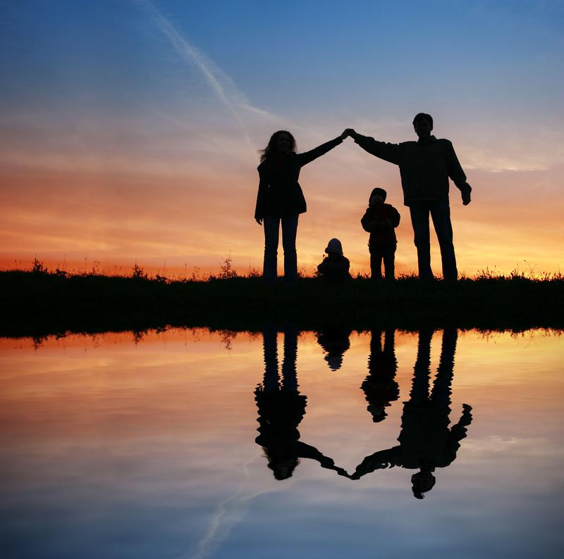 Silhouetted family holding hands by a reflective pond at sunset.