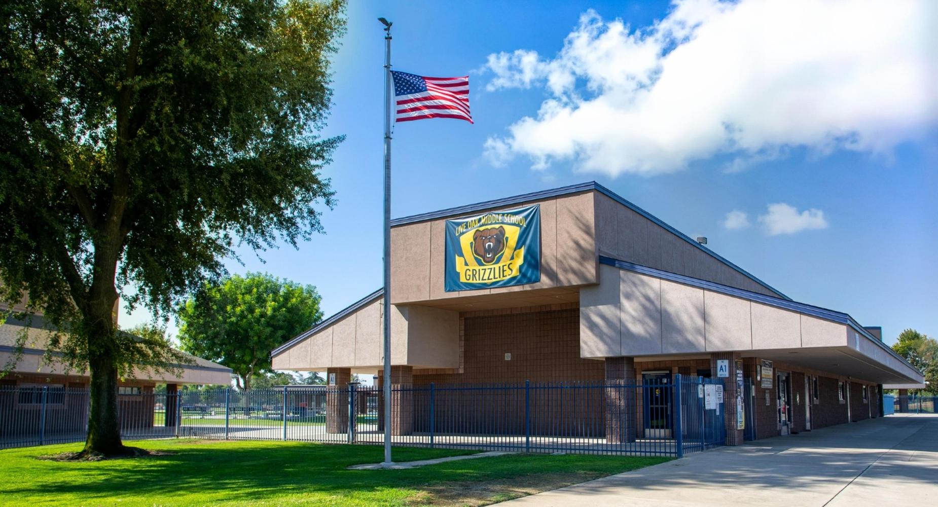 A school building with a grassy area, flagpole, and a banner featuring a grizzly bear.