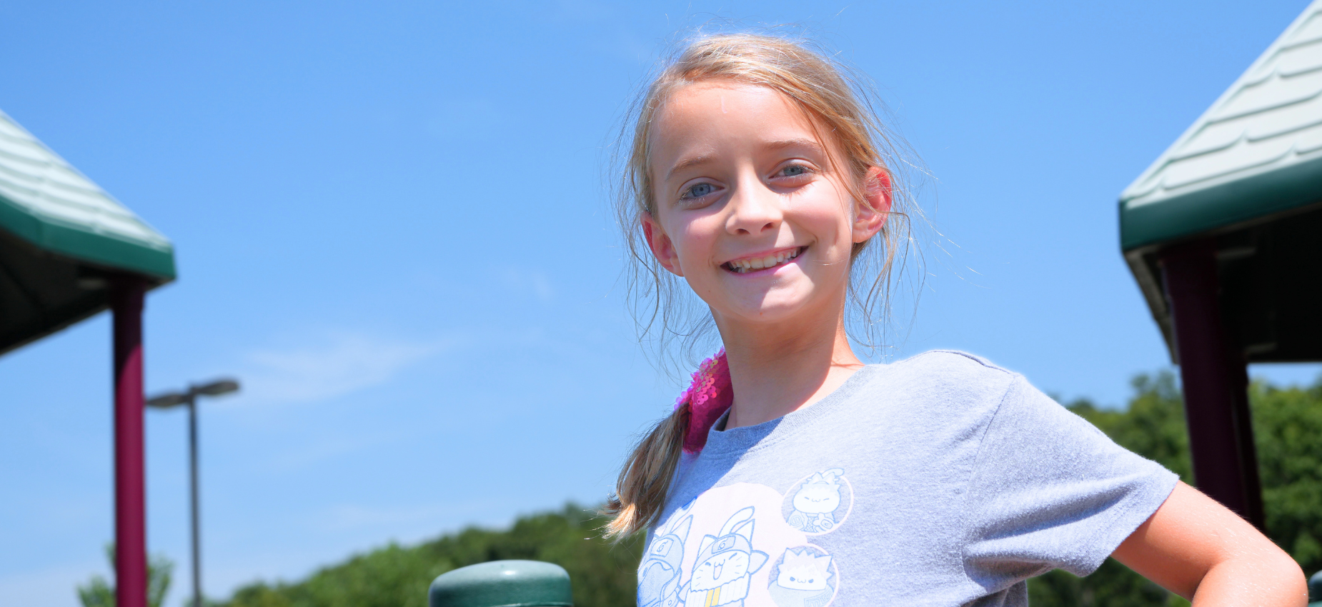 Smiling girl on a playground with a clear blue sky.