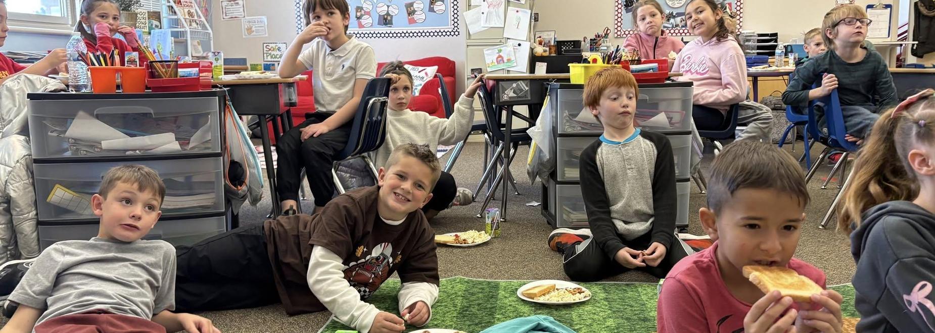 Children sitting on the floor in a classroom enjoying snacks.