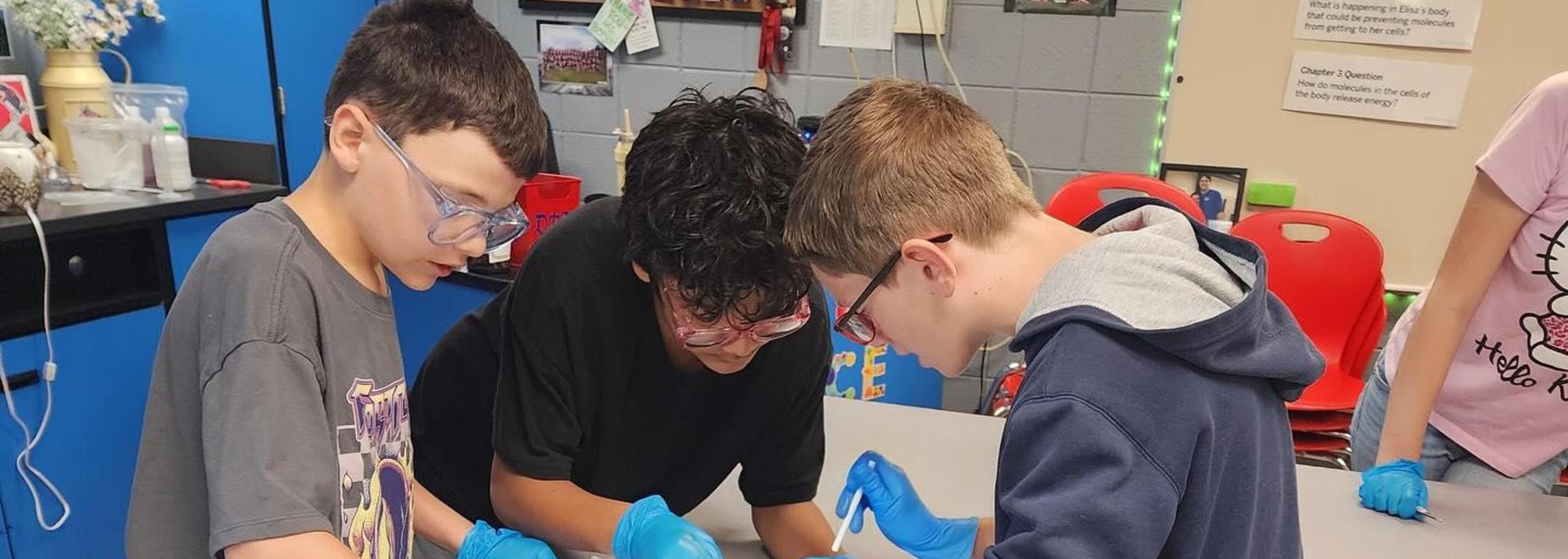 Children wearing gloves engaging in a hands-on activity at a classroom table.