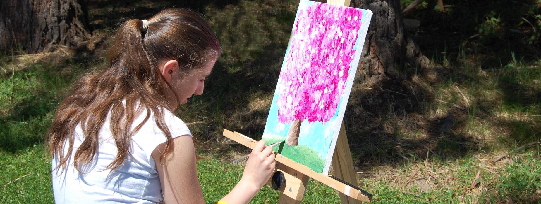 Student painting an apple tree in blossom at an easel outside.