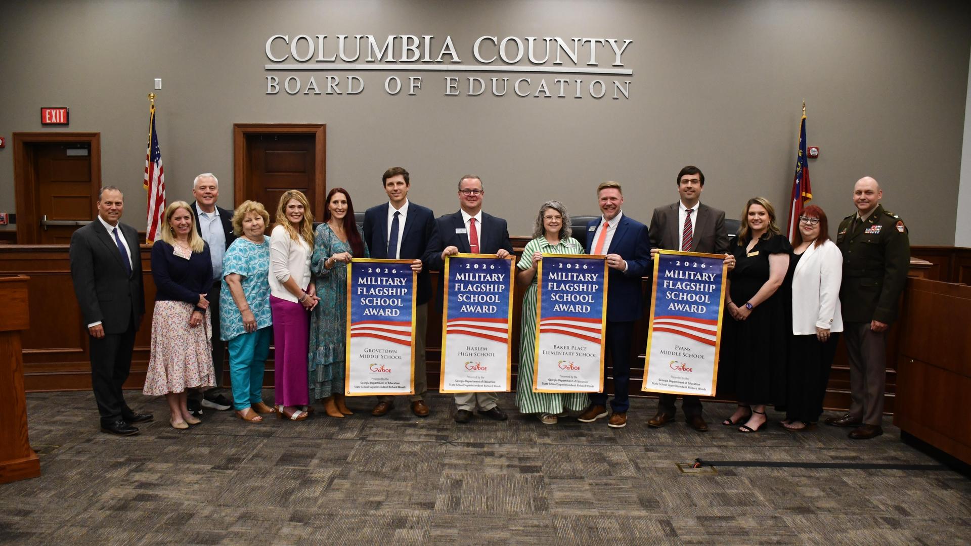 Group of people holding Military Flagship School Award banners at a board meeting.
