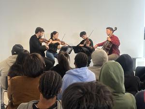 Four musicians playing string instruments in front of an audience.