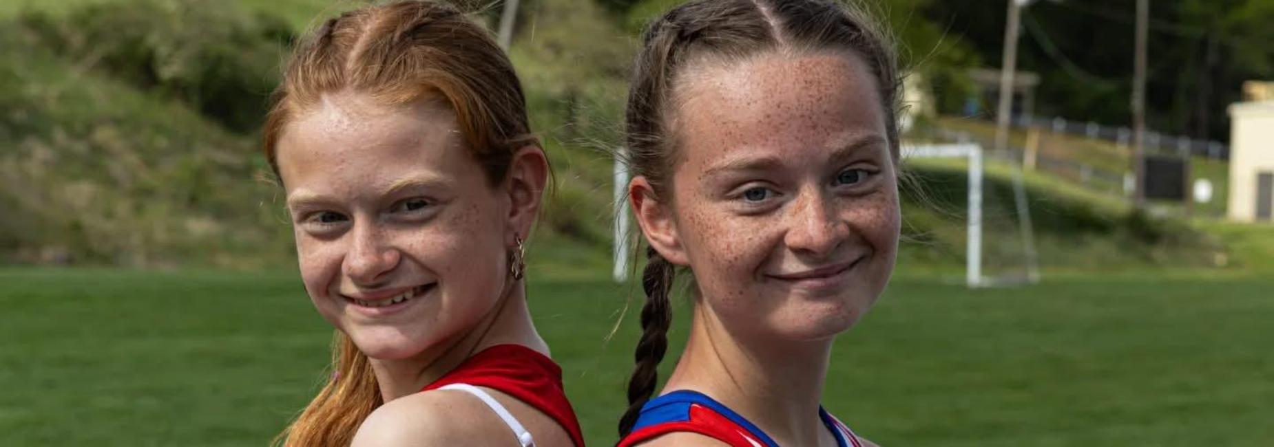 two girls in track uniforms standing back to back on the track.