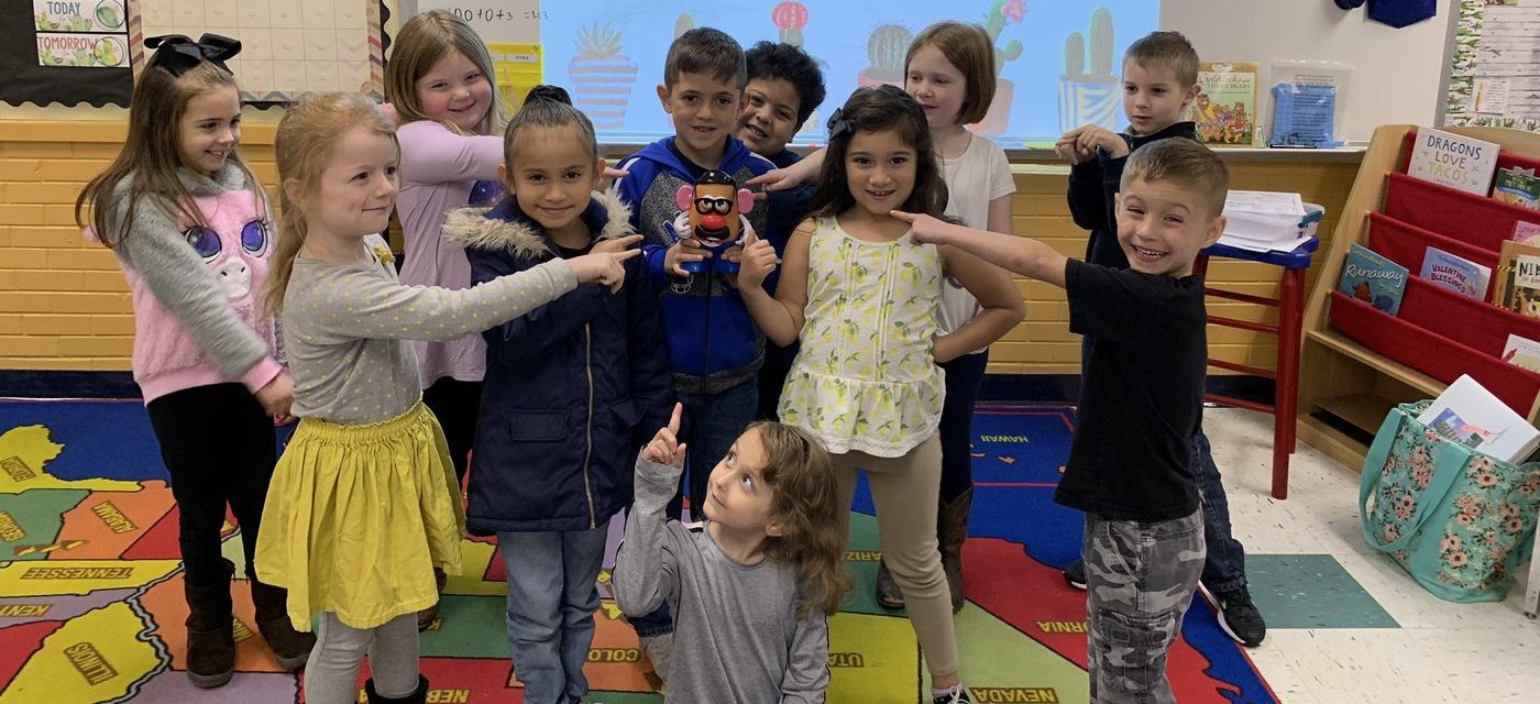 group of students all pose pointing at Mr. Potato Head