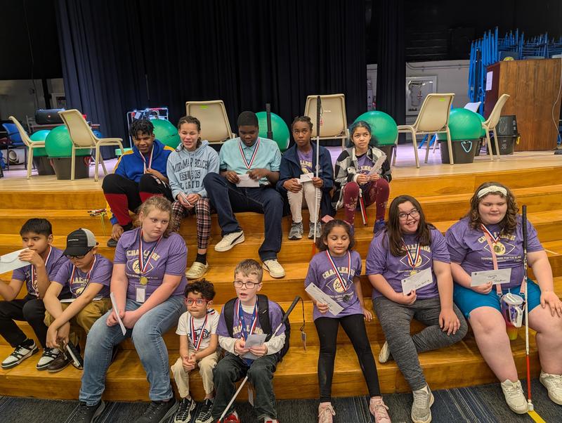 Students seated on stage steps with medals and certificates after the Braille Challenge.