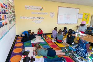 Arco Iris Spanish Immersion students sprawl out in groups on the carpeted floor of a colorful classroom and decorate huge pieces of poster board.