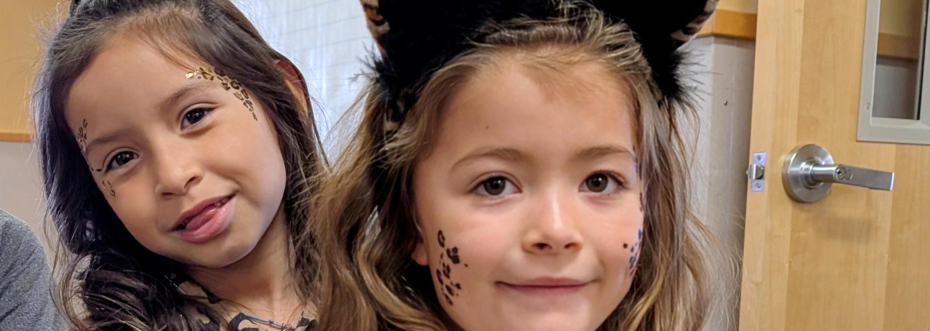 Child in a cat-themed sweatshirt with a friend in a leopard print top.