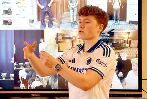 A student gestures while presenting in front of a large screen display.