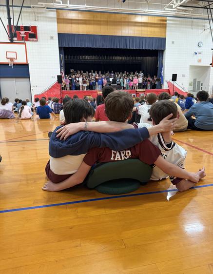 Three children sitting closely together at a school performance.