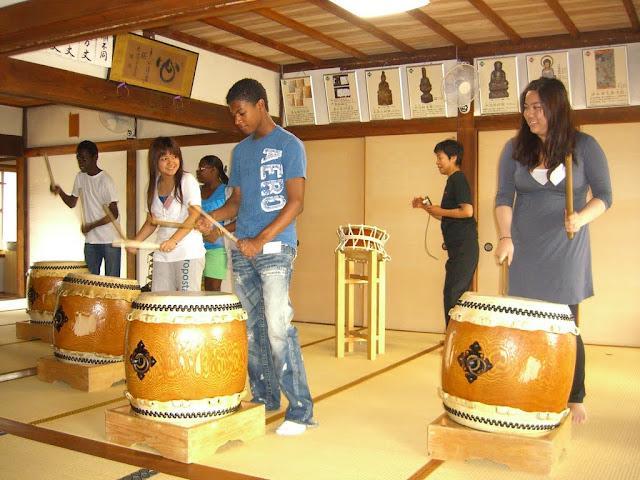 A group of people playing traditional Japanese taiko drums in a studio.