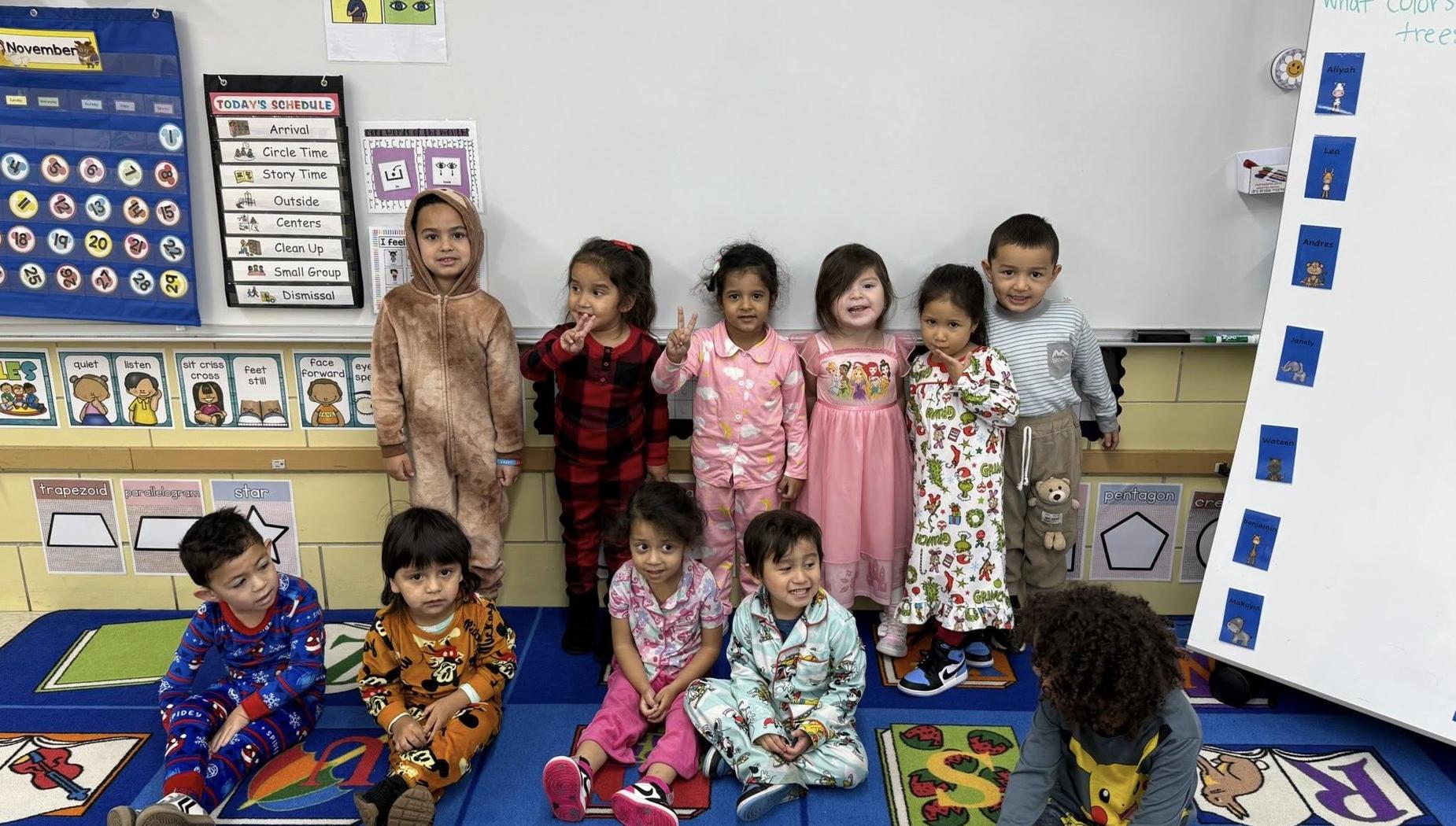A group of children in pajamas posing together in a colorful classroom setting.