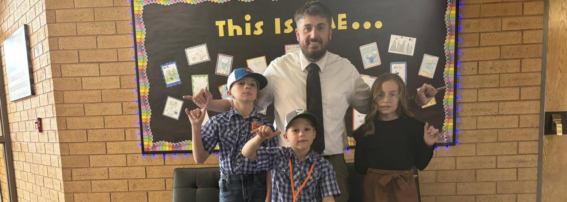 Three children standing in front of a wall, posing with a man in a suit behind them.