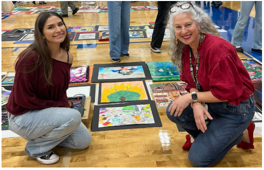 Student and teacher kneel on floor next to drawings and paintings