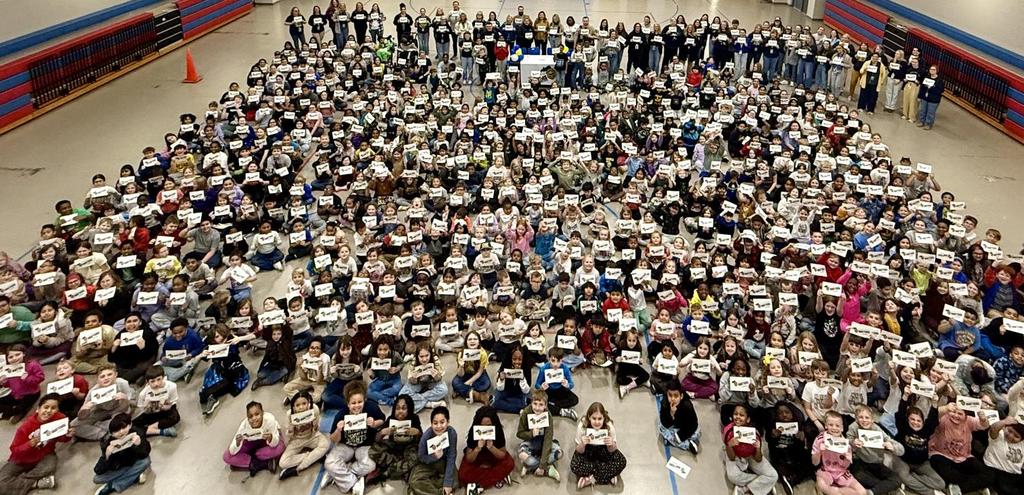 hundreds on students and adults sitting on gym floor holding up pledge signs