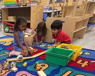 Three children playing with toys on a colorful rug in a classroom setting.