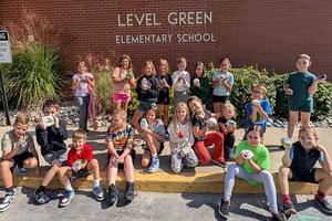 a large group of students stands outside a school and each one is holding a rock