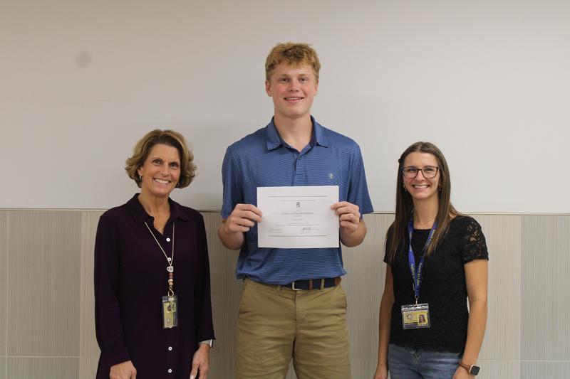 tall high school student holds certificate between two women science teachers