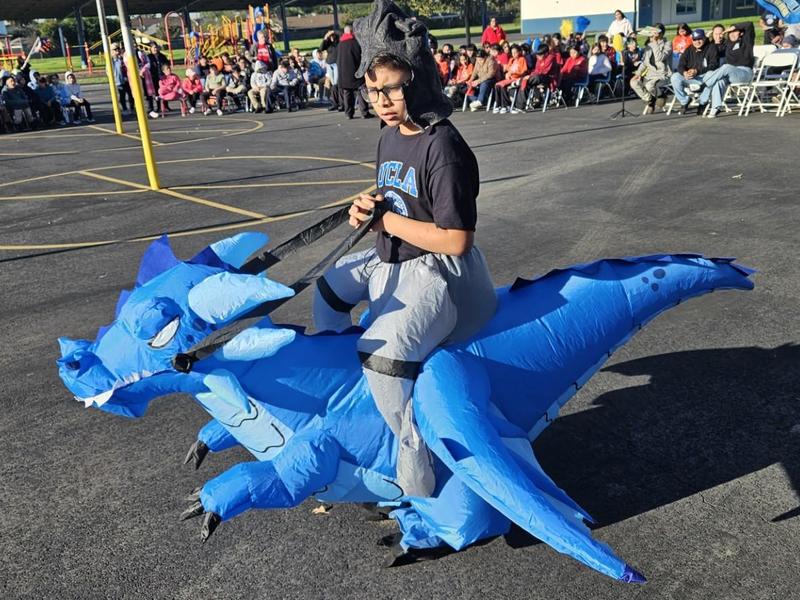 Child in a blue dragon costume sitting on an inflatable dragon.