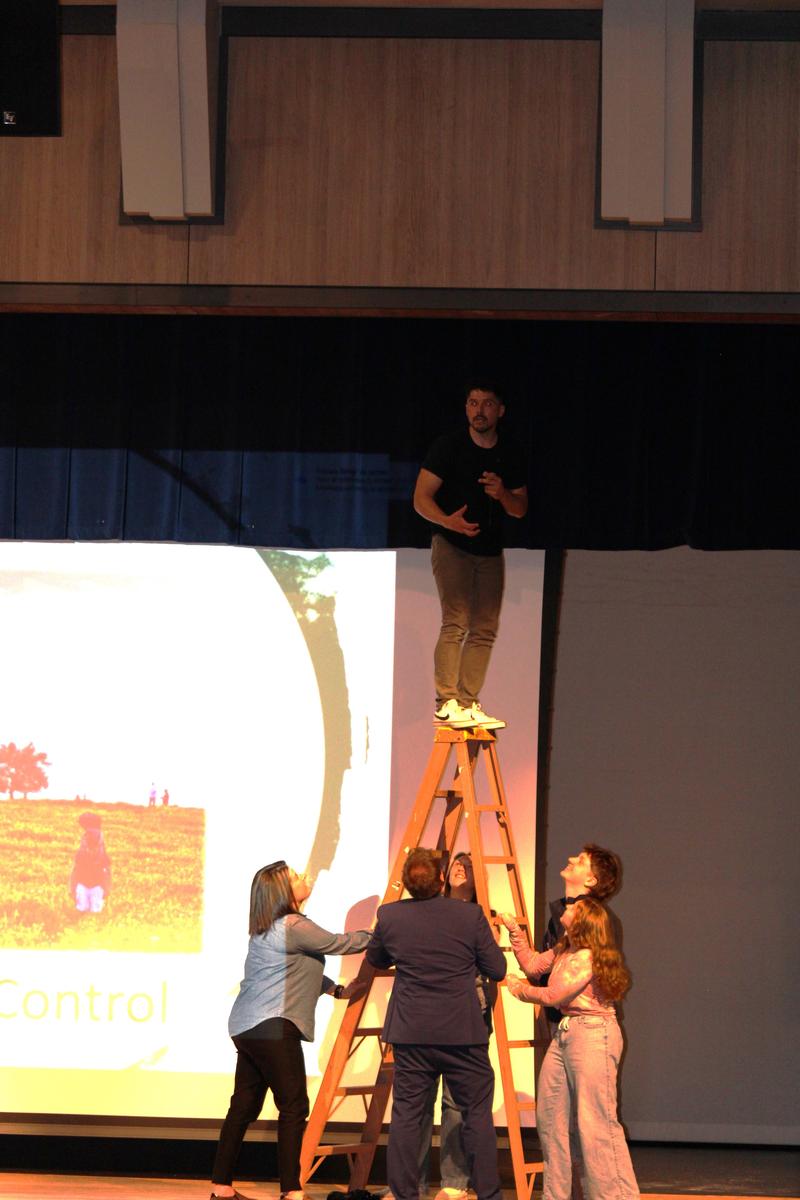 speaker standing on ladder while community supports the ladder
