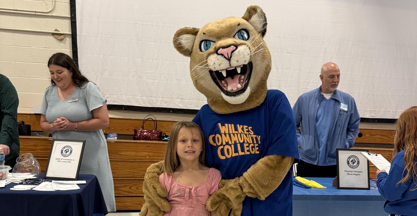 Child posing with a mascot in a college-themed setting.