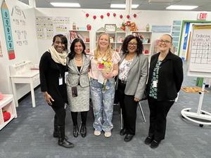 Teacher Katie Berry holds flowers surrounded by school and district leaders