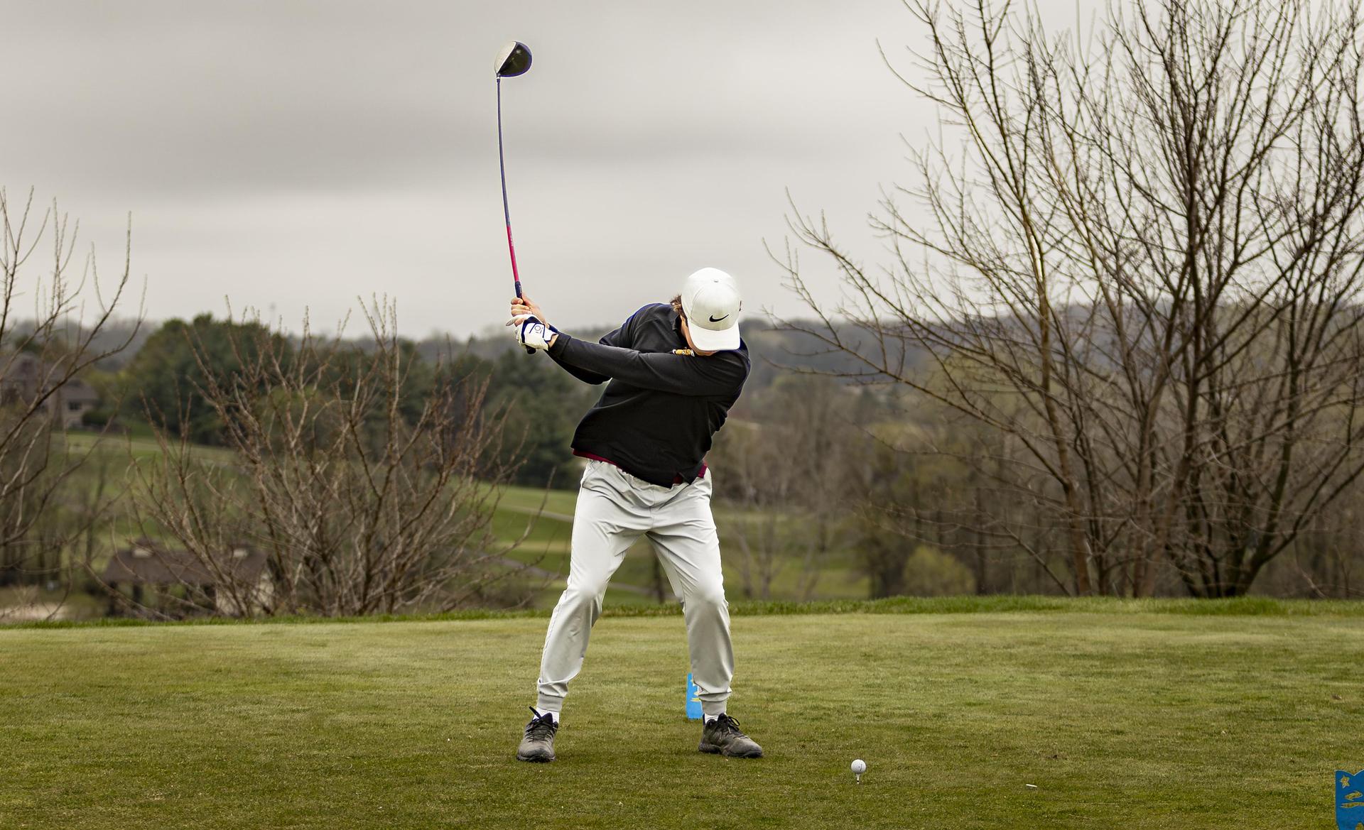 Golfer in a white hat swinging at the ball